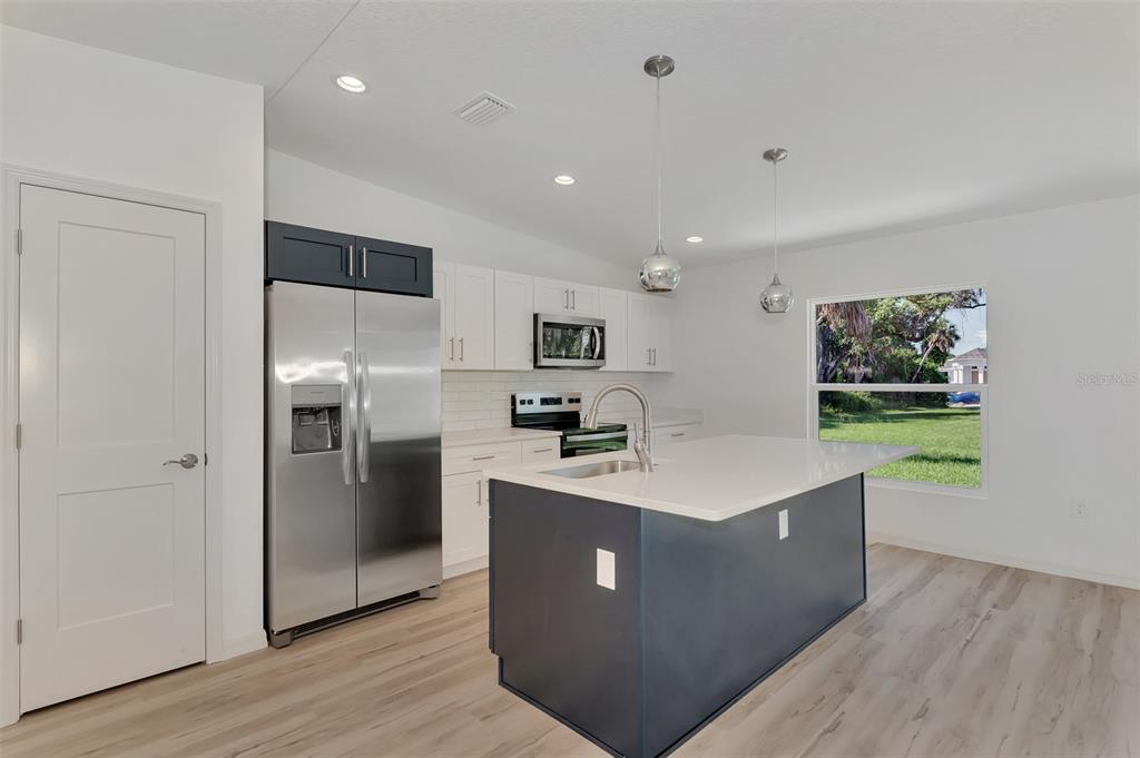 A modern kitchen features a dark blue island, white cabinetry, stainless steel appliances, and wood-look flooring — 3383 DRYDEN STREET, NORTH PORT, FL