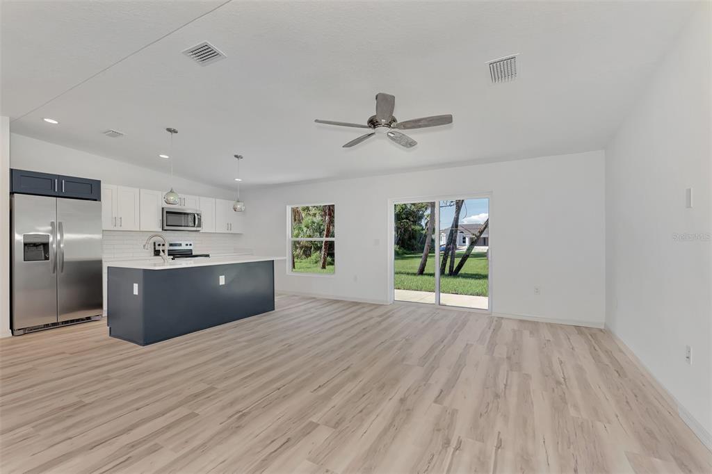 An open-concept kitchen and living area features white cabinets, a dark island, and wood-look flooring — 3383 DRYDEN STREET, NORTH PORT, FL