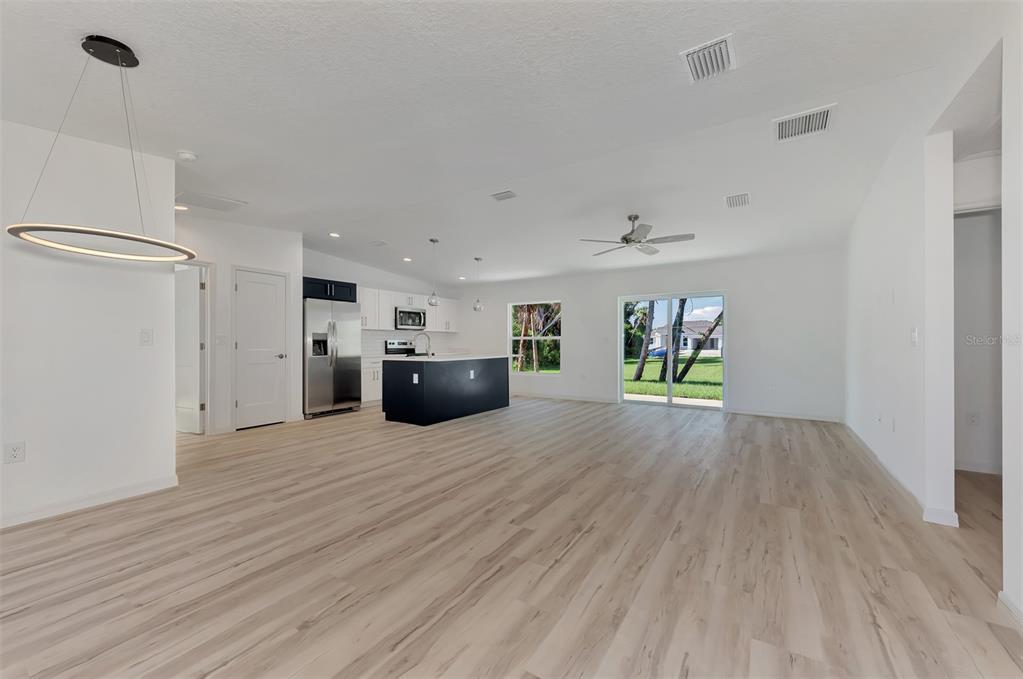 An open-concept kitchen and living area features light wood-look flooring, white walls, and a dark island — 3383 DRYDEN STREET, NORTH PORT, FL