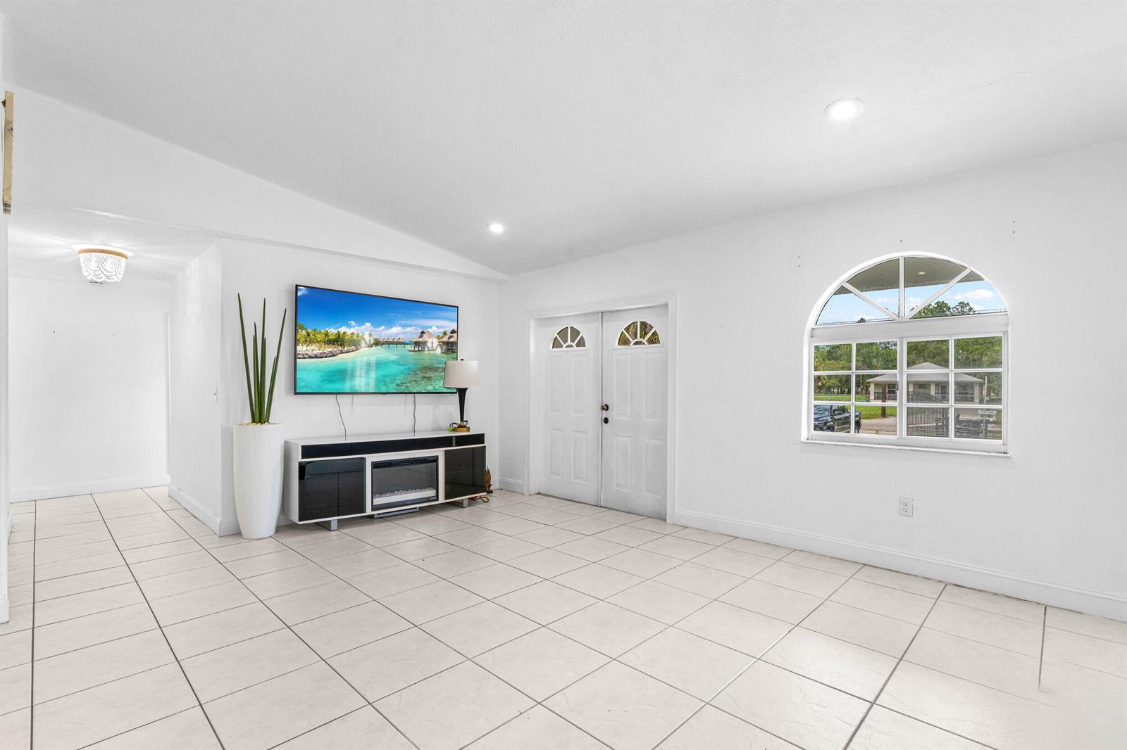 A bright living room features white walls, tiled floors, a wall-mounted television, and double doors — 340 S Arboleda Street, Clewiston FL 33440, CLEWISTON, FL