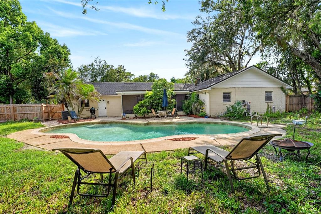 A backyard features a swimming pool, patio furniture, and a single-story house with trees — 209 ROYAL OAKS CIRCLE, LONGWOOD, FL