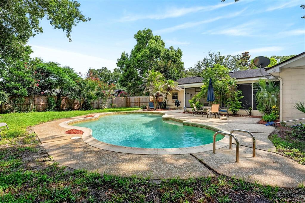 A backyard features a kidney-shaped swimming pool with a concrete deck and a wooden fence — 209 ROYAL OAKS CIRCLE, LONGWOOD, FL