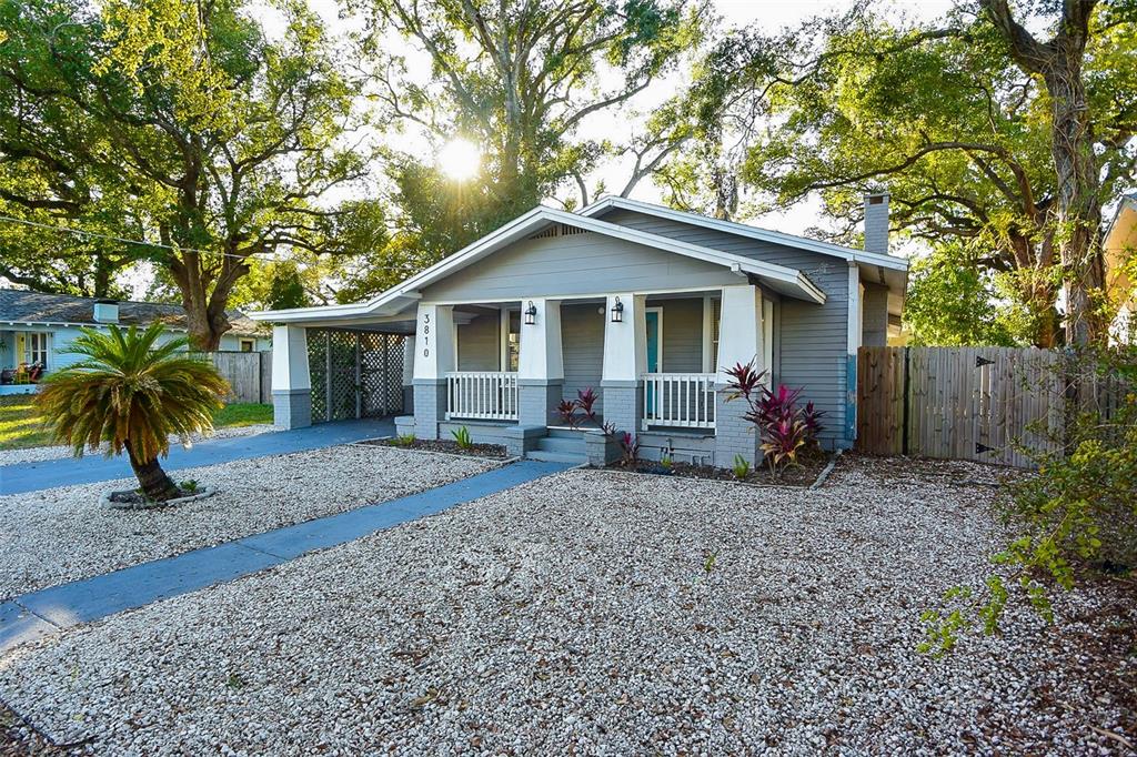 A gray, single-story house with a front porch, carport, and gravel yard under large trees — 3810 N ARLINGTON AVENUE, TAMPA, FL