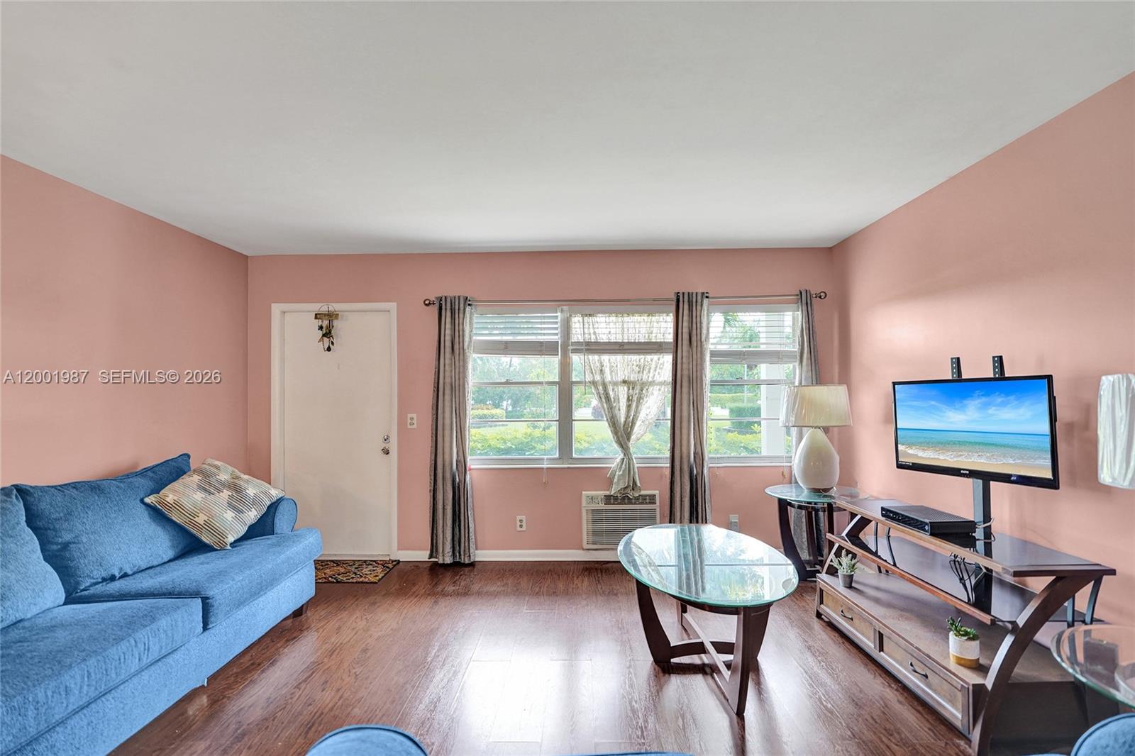 A living room features pink walls, dark wood flooring, a blue sofa, and a television — 511 Fanshaw M # 511, Boca Raton FL 33434, BOCA RATON, FL