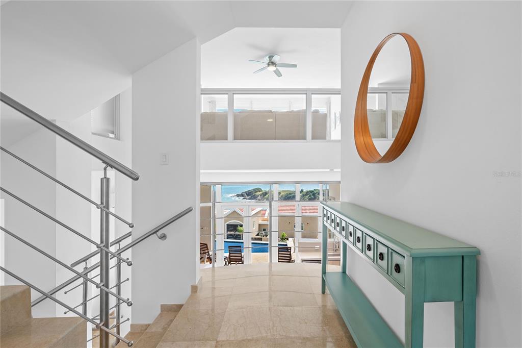 A staircase landing with a teal console table, oval mirror, and views of the ocean — 1 SHELL CASTLE CLUB UNIT 78, HUMACAO, PR