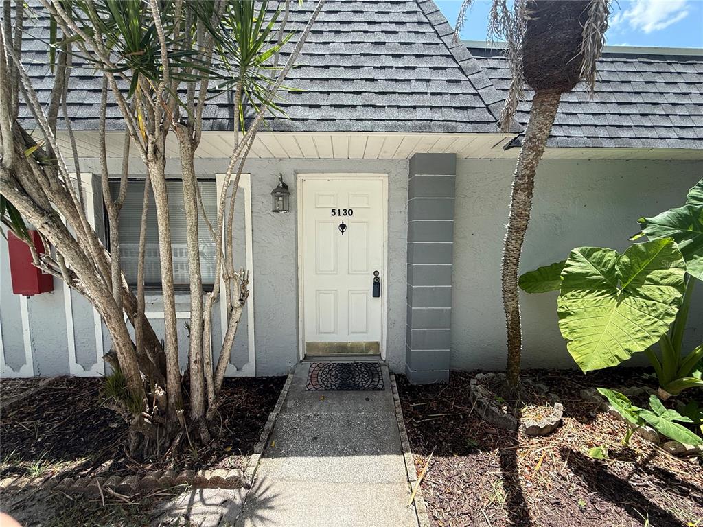 The exterior of a residential unit features a white front door, a walkway, and landscaping — 5130 70TH PLACE N, PINELLAS PARK, FL