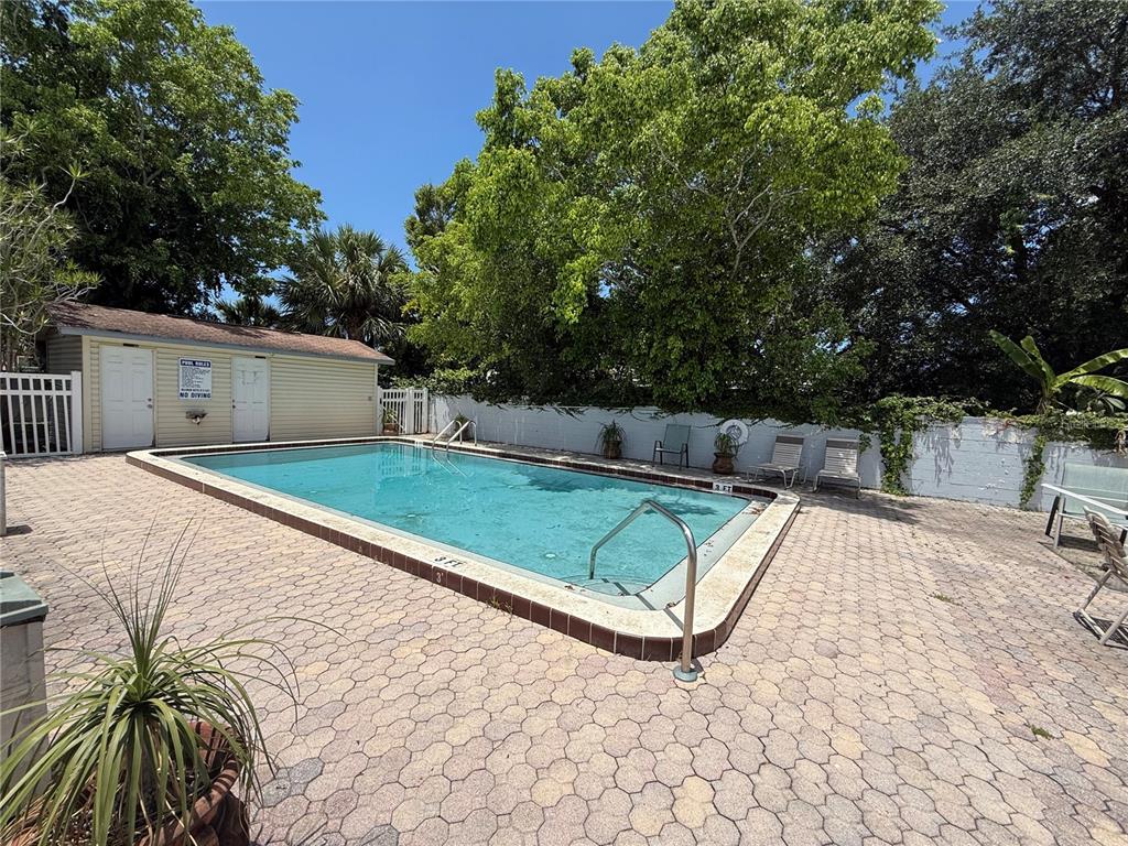 An outdoor rectangular swimming pool is surrounded by a paved patio and mature trees — 5130 70TH PLACE N, PINELLAS PARK, FL