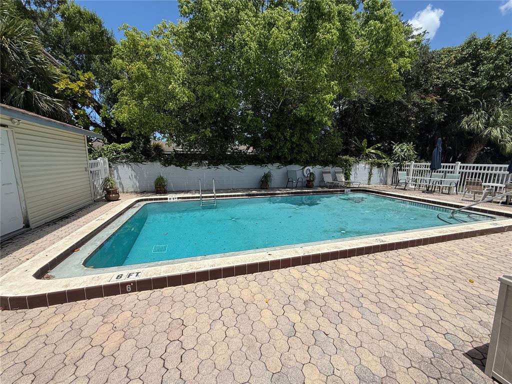 A rectangular swimming pool with a paved deck is surrounded by a white fence and trees — 5130 70TH PLACE N, PINELLAS PARK, FL