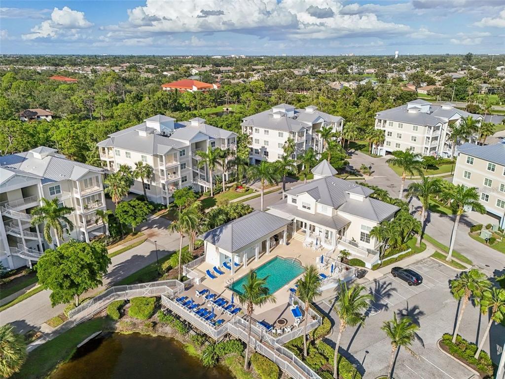 An aerial view shows a community pool and clubhouse surrounded by multi-story residential buildings — 3440 77TH STREET W UNIT 201, BRADENTON, FL