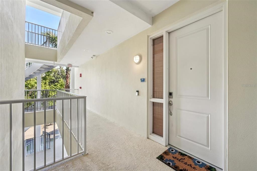 An exterior hallway leads to a white front door with a welcome mat — 3440 77TH STREET W UNIT 201, BRADENTON, FL