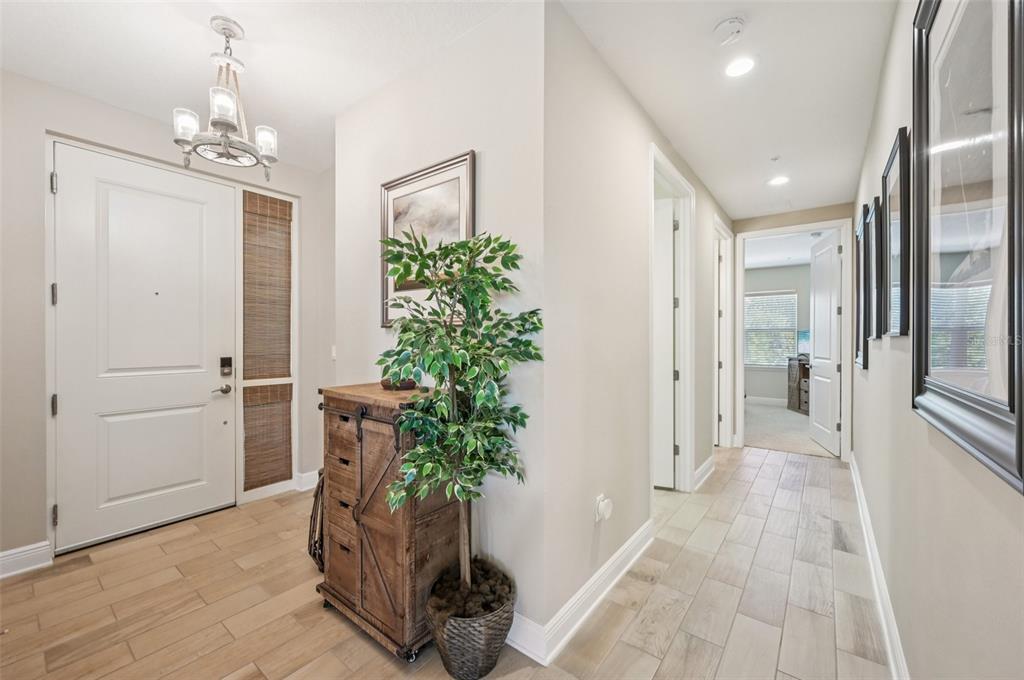 A bright entryway features light wood-look tile flooring, a rustic wooden cabinet, and a chandelier — 3440 77TH STREET W UNIT 201, BRADENTON, FL