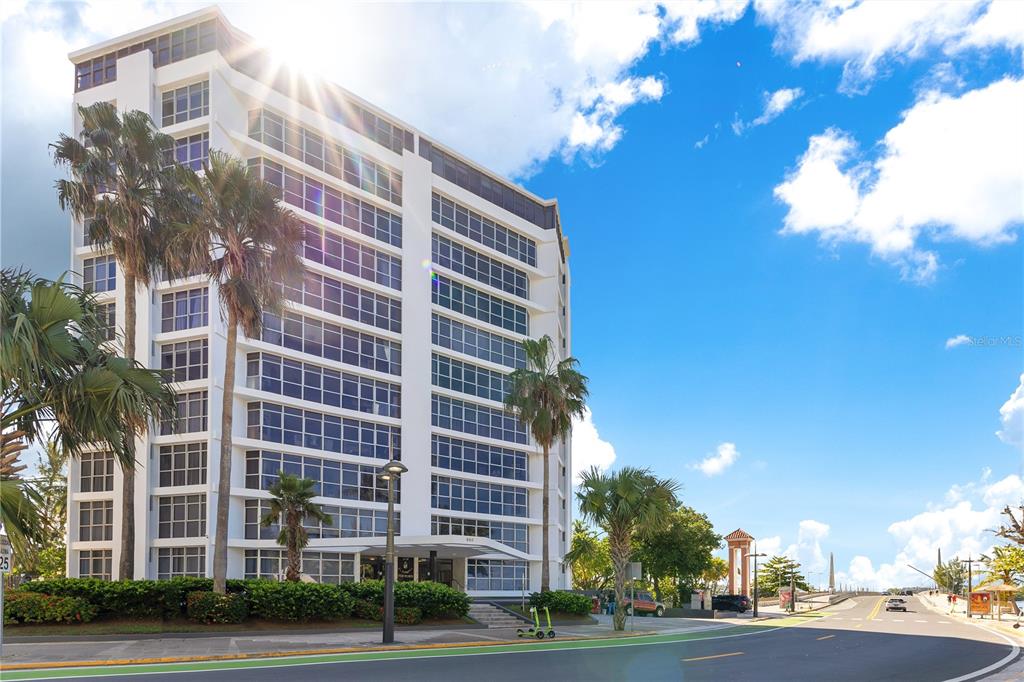 A multi-story white apartment building stands next to a road under a sunny sky — 800 ASHFORD AVENUE UNIT 6-B, SAN JUAN, PR