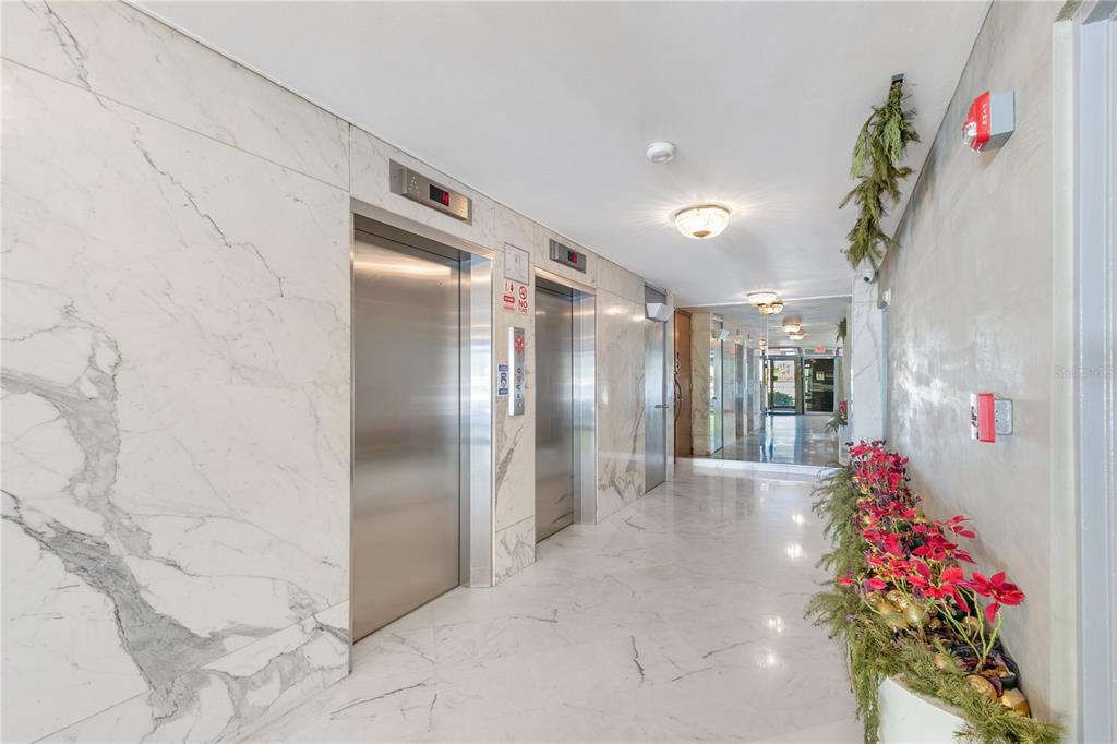 A marble-walled elevator lobby features two stainless steel elevators and a decorative floral arrangement — 800 ASHFORD AVENUE UNIT 6-B, SAN JUAN, PR