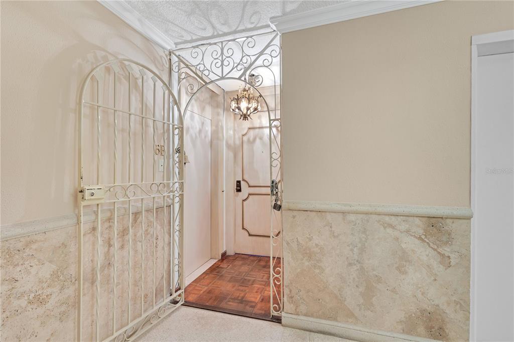 A white metal security gate opens to an entryway with marble wainscoting and a chandelier — 800 ASHFORD AVENUE UNIT 6-B, SAN JUAN, PR