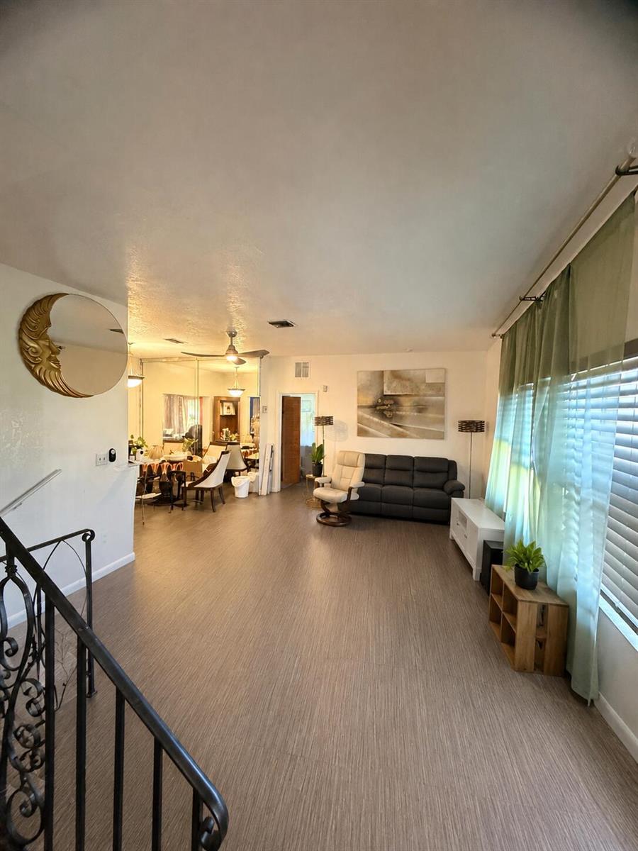A living room with wood-look flooring, a dark sofa, a recliner, and a crescent moon wall decoration — 19720 NW 12th Court, Miami FL 33169, MIAMI, FL