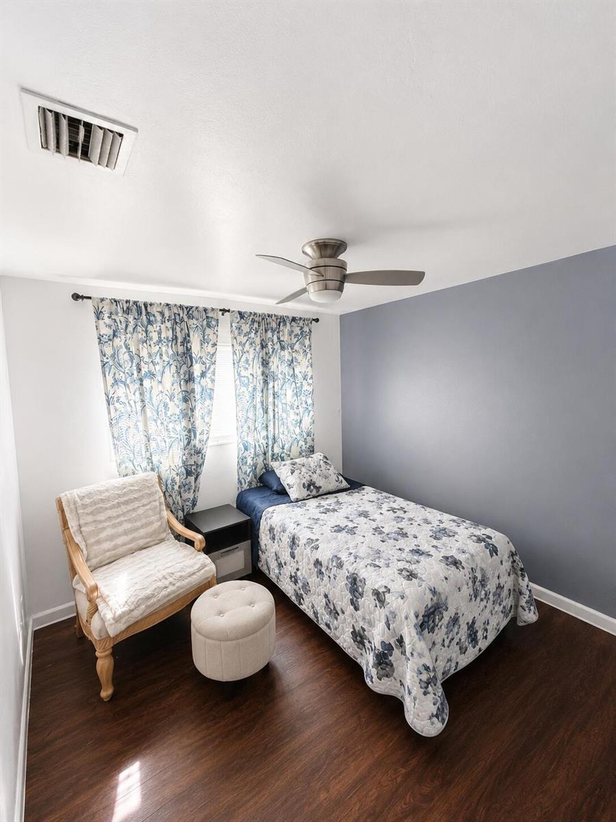 A bedroom features a twin bed, a patterned armchair with an ottoman, and dark flooring — 19720 NW 12th Court, Miami FL 33169, MIAMI, FL