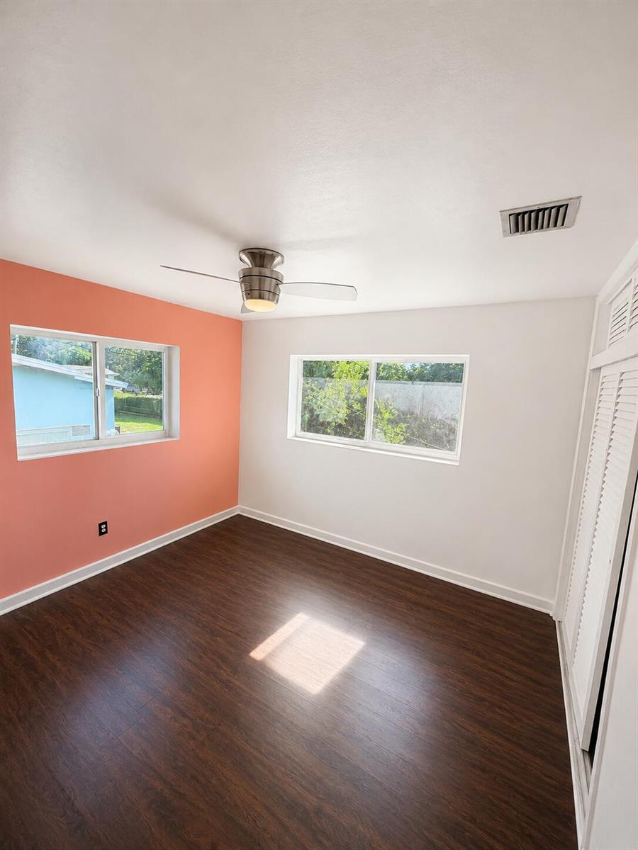 A bedroom with dark wood flooring, a coral accent wall, and a ceiling fan — 19720 NW 12th Court, Miami FL 33169, MIAMI, FL