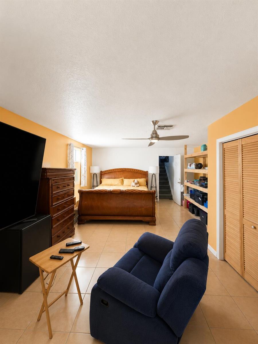 A bedroom with tile floors, a wooden bed frame, a blue recliner, and open shelving — 19720 NW 12th Court, Miami FL 33169, MIAMI, FL