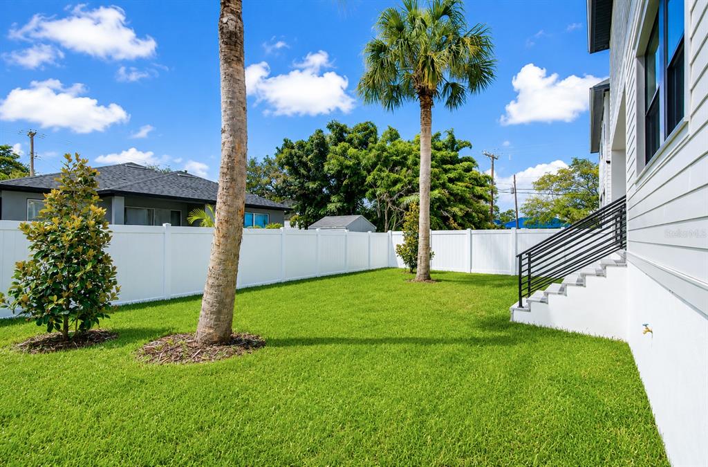 A grassy backyard features a white vinyl fence, two palm trees, and a house exterior — 7303 S FITZGERALD STREET, TAMPA, FL