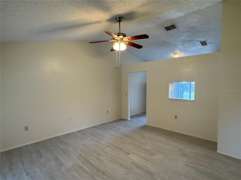 An empty room with vaulted ceilings, a ceiling fan, and light-colored wood-look flooring — 10041 MASSEY STREET, ORLANDO, FL