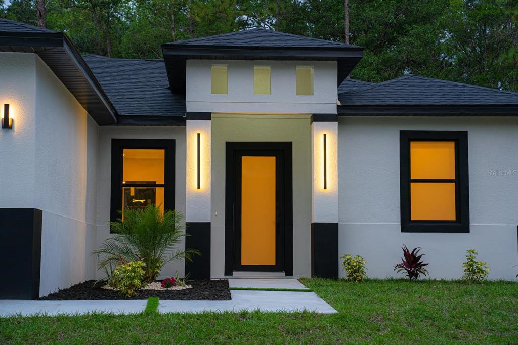 The exterior of a modern house features a white stucco facade, black trim, and lighting — 14284 CEDARWOOD AVENUE, BROOKSVILLE, FL