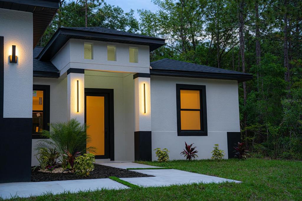 The exterior of a modern white house features black trim, vertical wall lights, and landscaping — 14284 CEDARWOOD AVENUE, BROOKSVILLE, FL