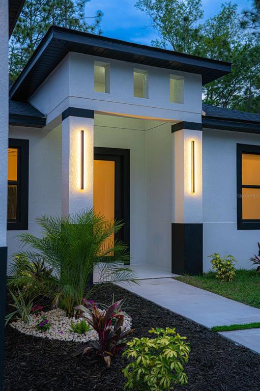The exterior of a modern white house features a covered entryway with vertical wall lights — 14284 CEDARWOOD AVENUE, BROOKSVILLE, FL