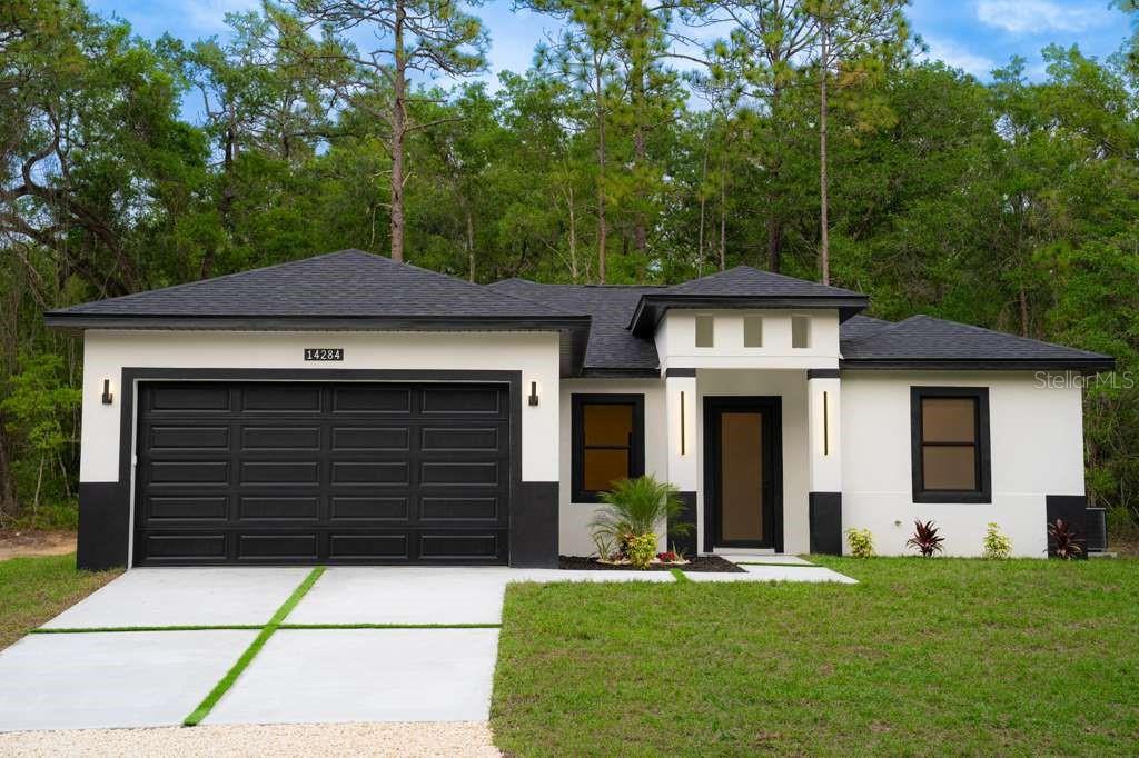 A modern single-story house with a black garage door and white stucco exterior — 14284 CEDARWOOD AVENUE, BROOKSVILLE, FL