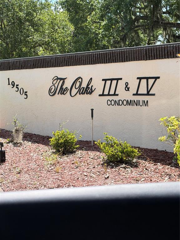 A beige stucco wall displays the black metal sign for The Oaks III & IV Condominium — 19505 QUESADA AVENUE UNIT U204, PORT CHARLOTTE, FL
