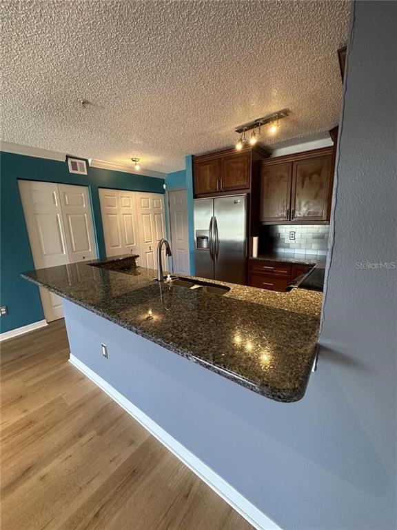 A kitchen features dark wood cabinets, granite countertops, a stainless steel refrigerator, and blue walls — 2400 FEATHER SOUND DRIVE UNIT 1435, CLEARWATER, FL