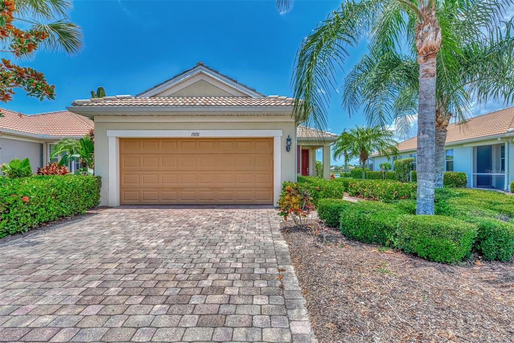 A beige house with a tan garage door and a paved driveway under a blue sky — 19191 LAPPACIO STREET, VENICE, FL