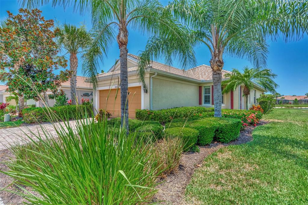 A single-story house with a tan stucco exterior, a two-car garage, and surrounding palm trees — 19191 LAPPACIO STREET, VENICE, FL