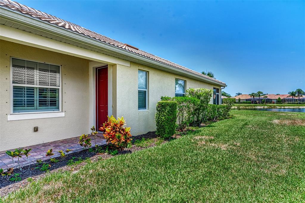 A side view of a beige house with a red door and a grassy lawn — 19191 LAPPACIO STREET, VENICE, FL