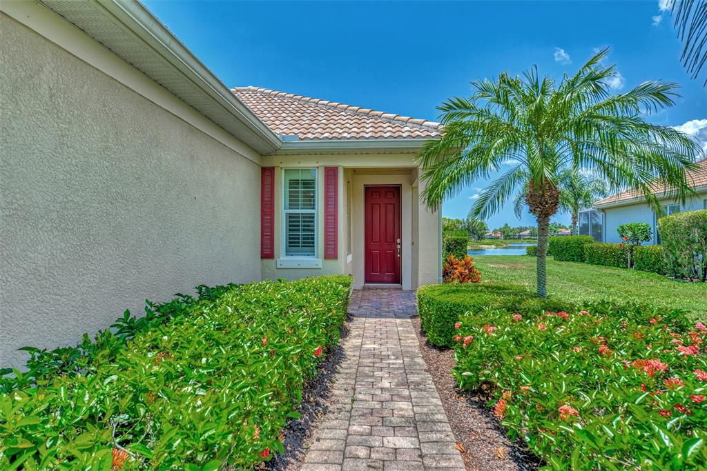 A brick walkway leads to the red front door of a house with landscaped bushes — 19191 LAPPACIO STREET, VENICE, FL