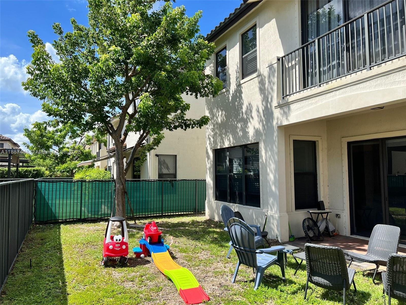 A backyard features a small slide, a toy car, patio chairs, and a two-story house — 3214 W 97th St, Hialeah FL 33018, HIALEAH, FL