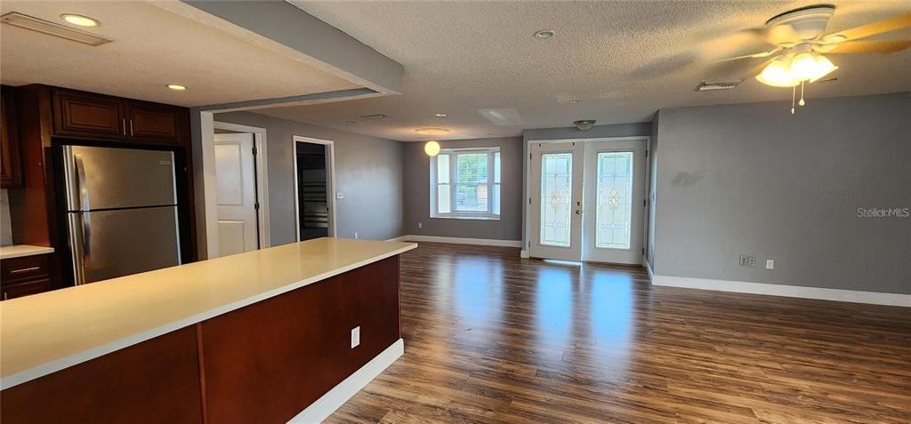 A kitchen island overlooks a living area with wood-look flooring and double glass doors — 2408 KIMBERLY DRIVE, DELTONA, FL
