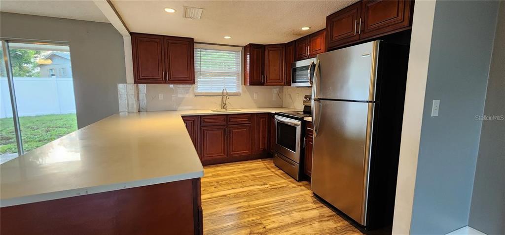 A kitchen features dark wood cabinets, stainless steel appliances, and a white countertop peninsula — 2408 KIMBERLY DRIVE, DELTONA, FL