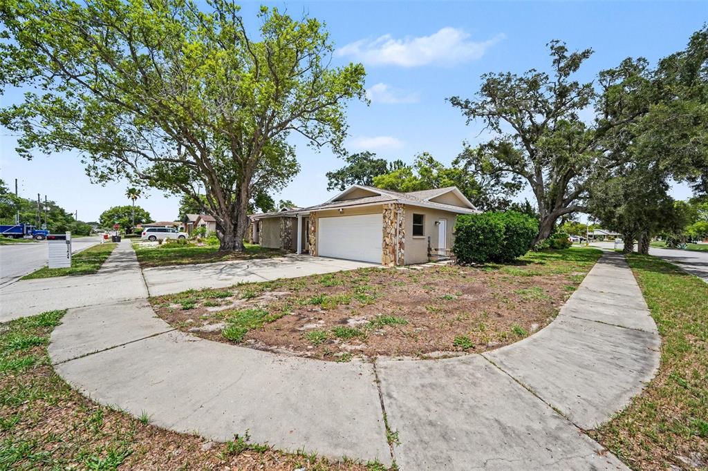 A single-story house with a white garage door and stone accents sits on a corner lot — 11424 SCALLOP DRIVE, PORT RICHEY, FL