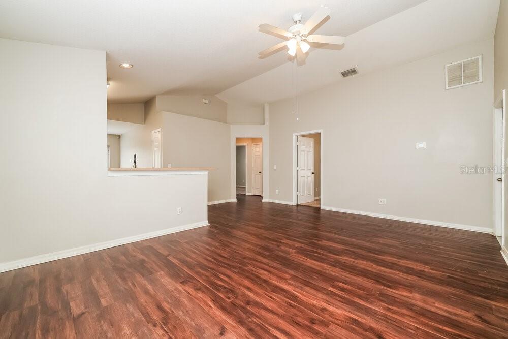 An empty living room features vaulted ceilings, a ceiling fan, and dark wood-look flooring — 10523 LAKESIDE VISTA DRIVE, RIVERVIEW, FL