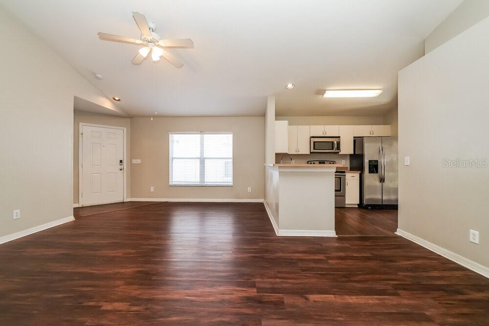 An open-concept living area with wood-look flooring, a ceiling fan, and an adjacent kitchen — 10523 LAKESIDE VISTA DRIVE, RIVERVIEW, FL