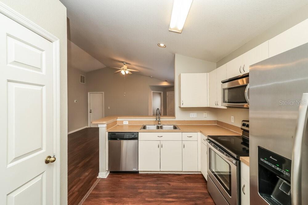 A kitchen with white cabinets, stainless steel appliances, and wood-look flooring opens to a living area — 10523 LAKESIDE VISTA DRIVE, RIVERVIEW, FL