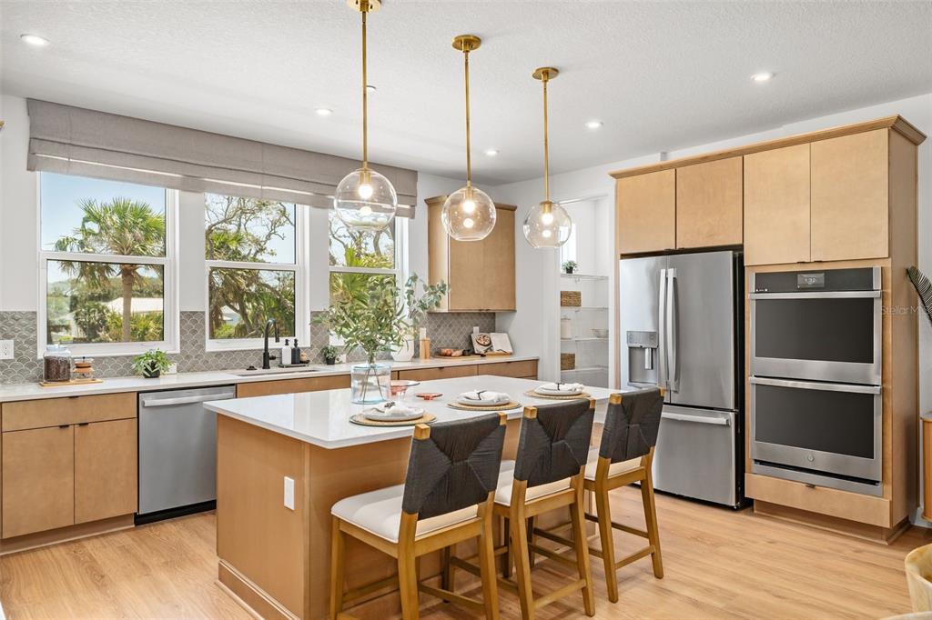 A modern kitchen features light wood cabinets, a white quartz island, and three glass pendant lights — 4105 TIDEWATCH LOOP, NEW SMYRNA BEACH, FL
