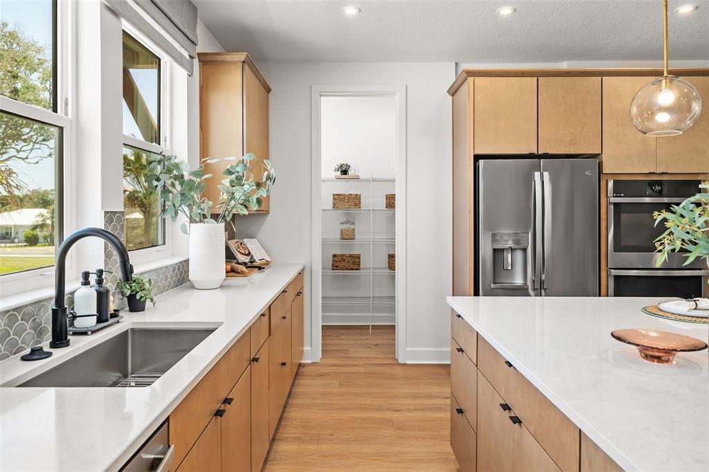 A modern kitchen features light wood cabinets, white countertops, a stainless steel refrigerator, and a pantry — 4105 TIDEWATCH LOOP, NEW SMYRNA BEACH, FL