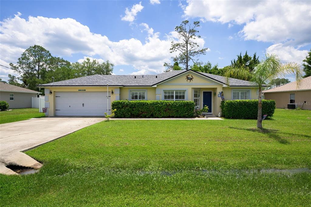 A single-story house with a white garage, yellow siding, and a manicured hedge in front — 18 PHOENIX LANE, PALM COAST, FL