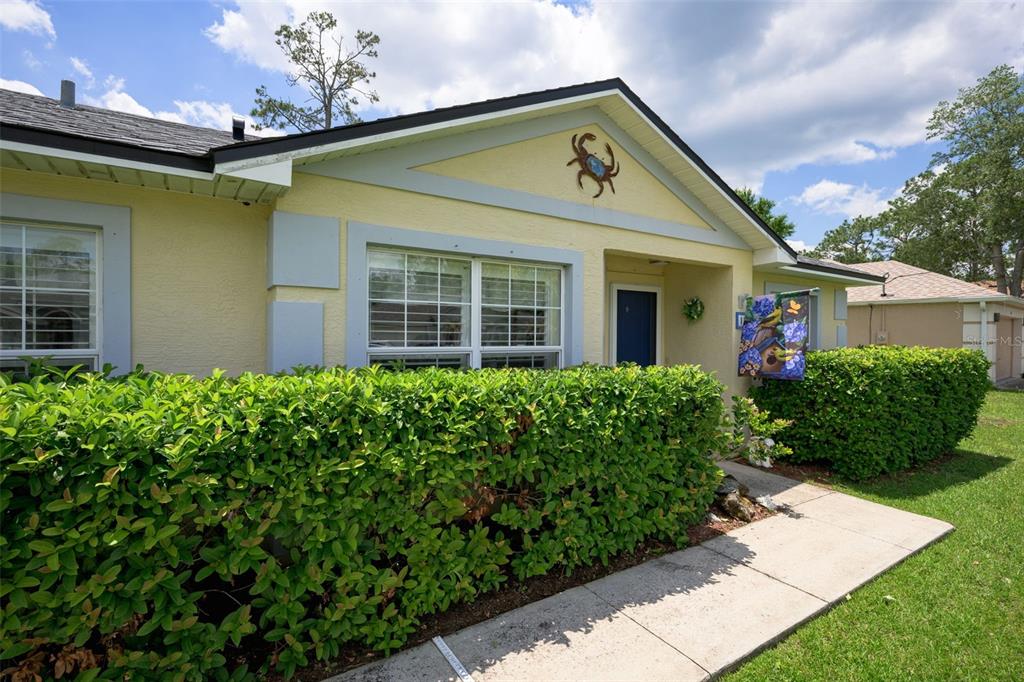 A yellow house exterior features a crab wall decoration, a hedge, and a concrete walkway — 18 PHOENIX LANE, PALM COAST, FL