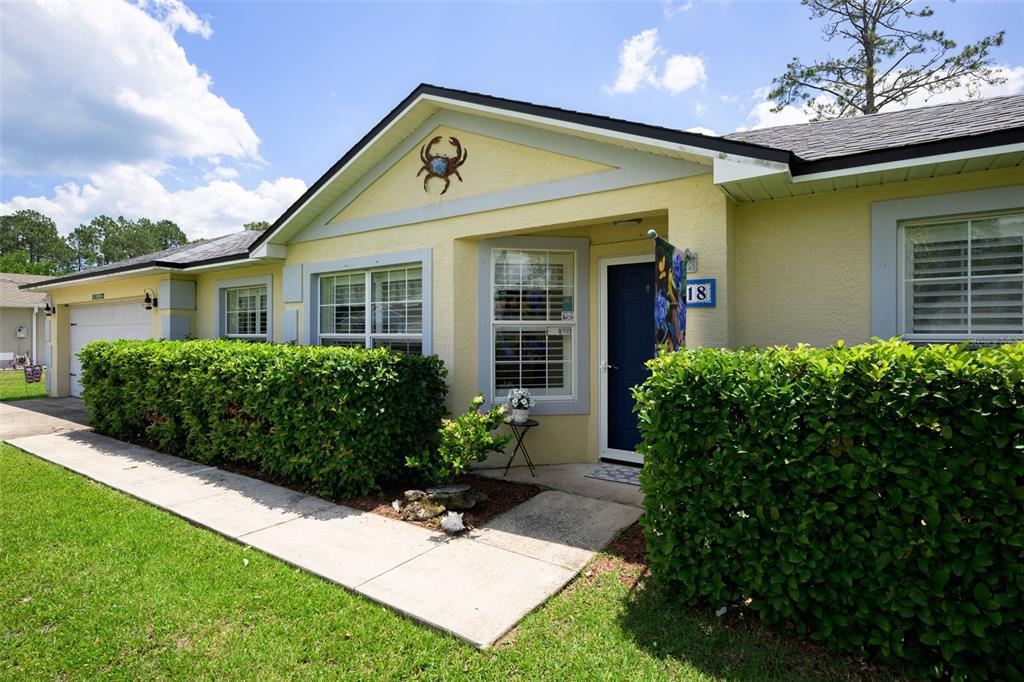 A yellow house exterior features a crab wall decoration, a blue front door, and hedges — 18 PHOENIX LANE, PALM COAST, FL