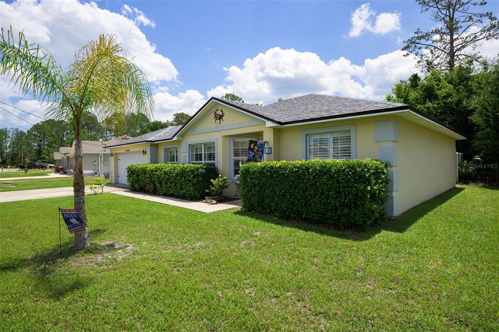 A single-story house with yellow stucco siding, a gray shingled roof, and a manicured hedge — 18 PHOENIX LANE, PALM COAST, FL