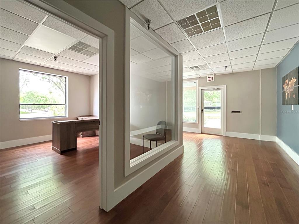 An office interior features wood flooring, a glass-walled conference room, and an exit door — 2441 NW 43RD STREET UNIT 5B, GAINESVILLE, FL