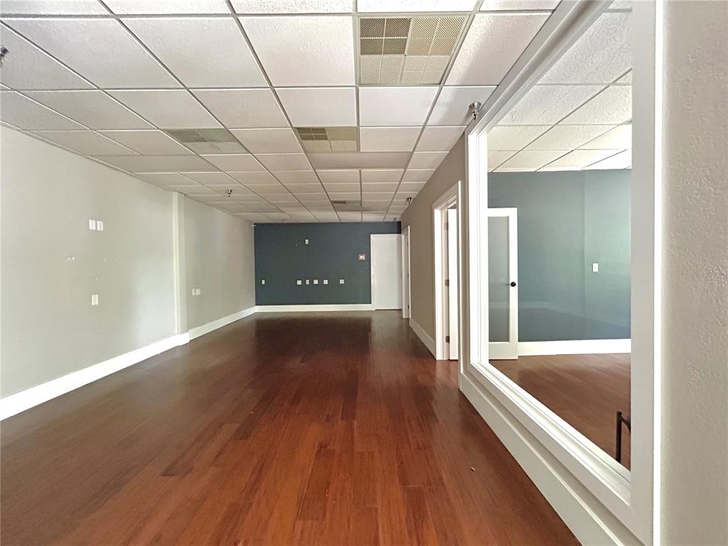 An empty office space features wood flooring, a drop ceiling, and a large interior window — 2441 NW 43RD STREET UNIT 5B, GAINESVILLE, FL