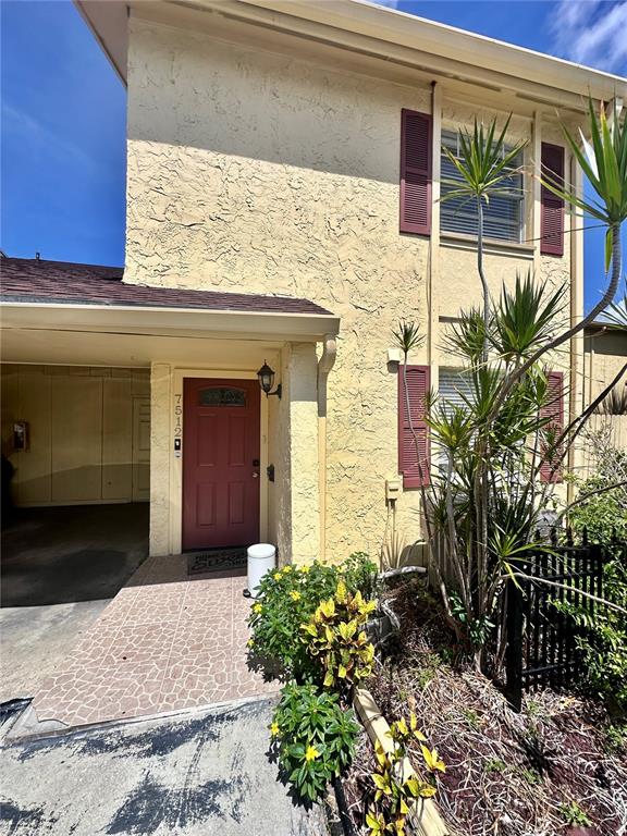 A beige two-story townhouse exterior features a red front door and a covered carport — 7512 BOLANOS COURT UNIT 7512, TAMPA, FL